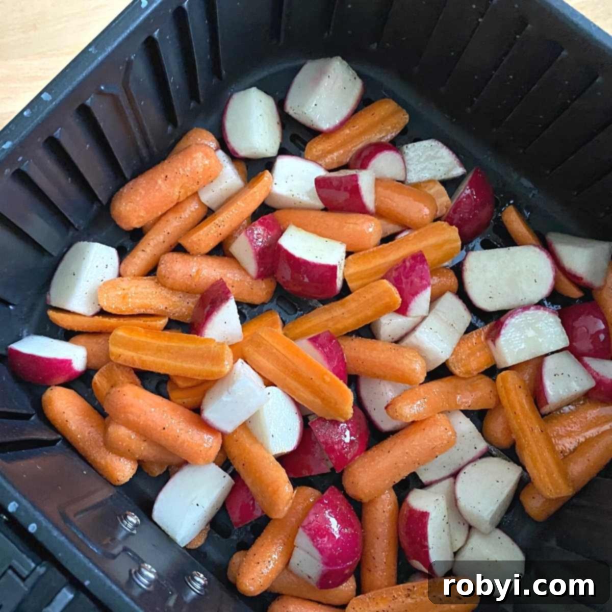 A close-up photograph of seasoned carrots and radishes meticulously arranged in an air fryer basket, perfectly positioned and ready for cooking to achieve optimal crispness.