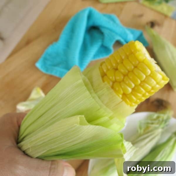Microwave Corn on the Cob being pulled from husk with hand.