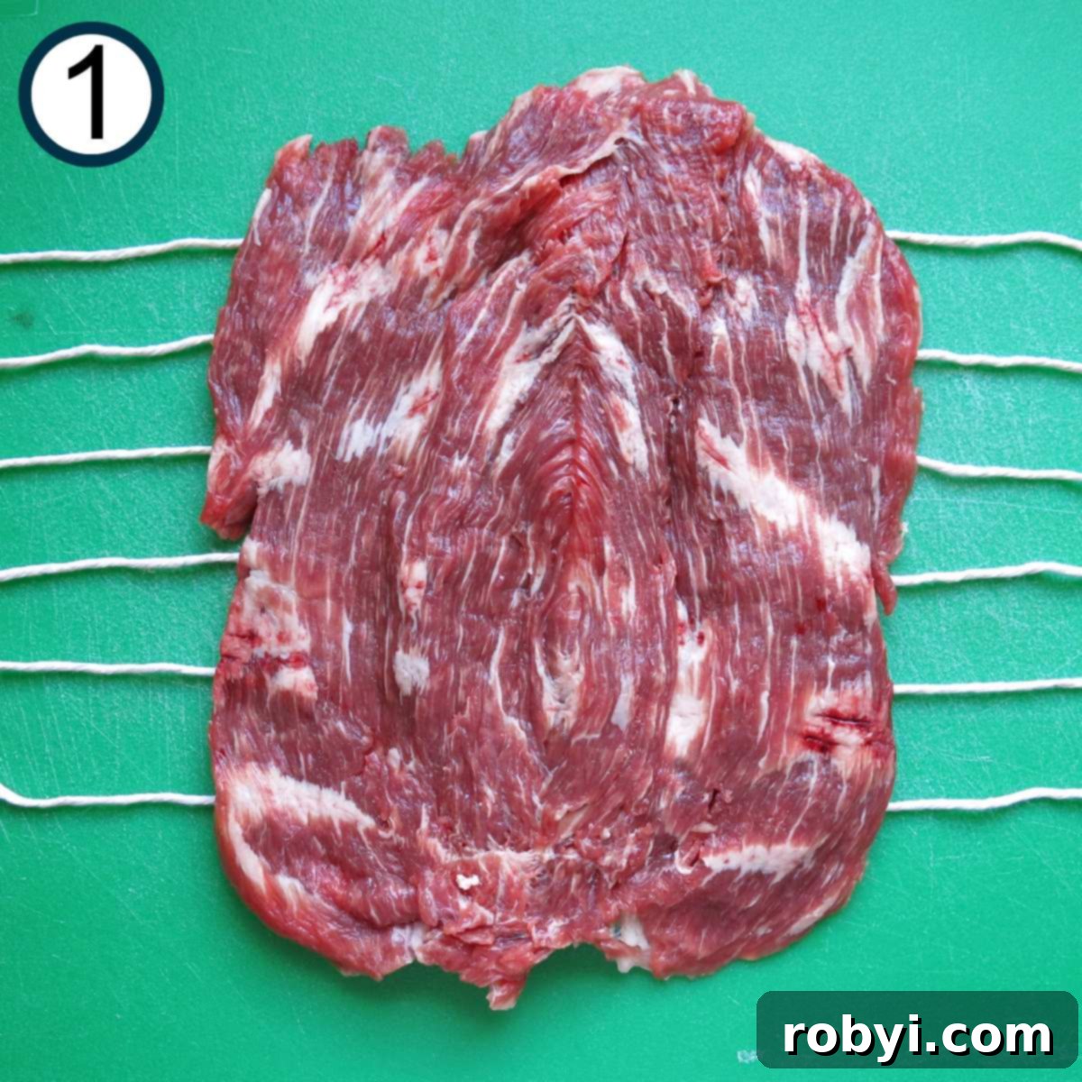 Butterflied flank steak on top of twine that's extended about 2 inches from the end of the meat.