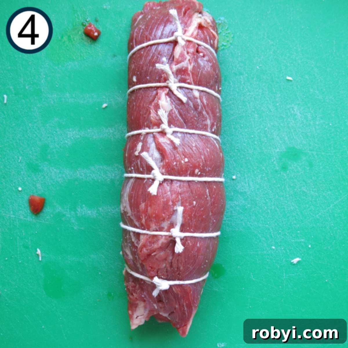 Rolled flank steak with pieces of twine tied at one inch intervals.