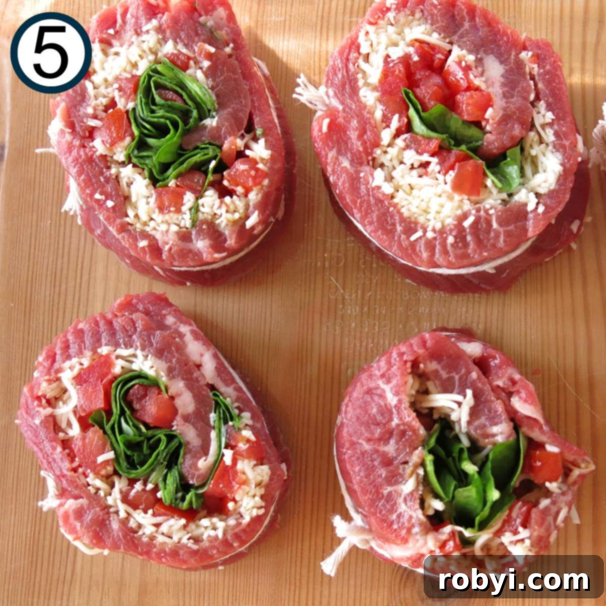 Four uncooked spinach stuffed steak pinwheels in a baking dish.