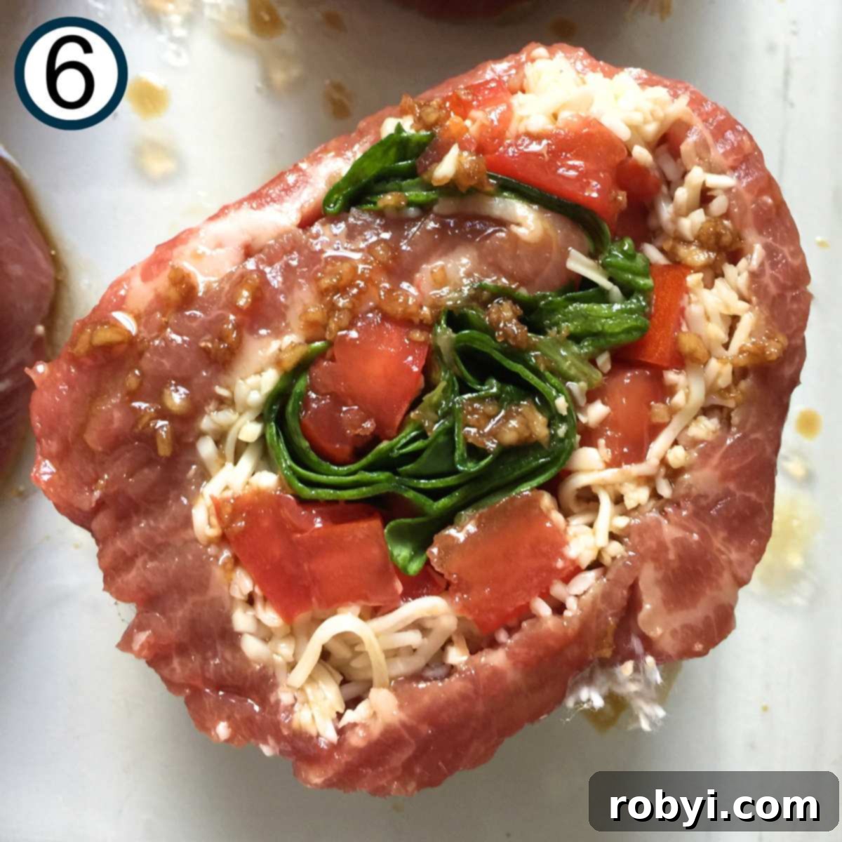 Close up of a cooked flank steak pinwheel stuffed with spinach, cheese, and tomatoes.