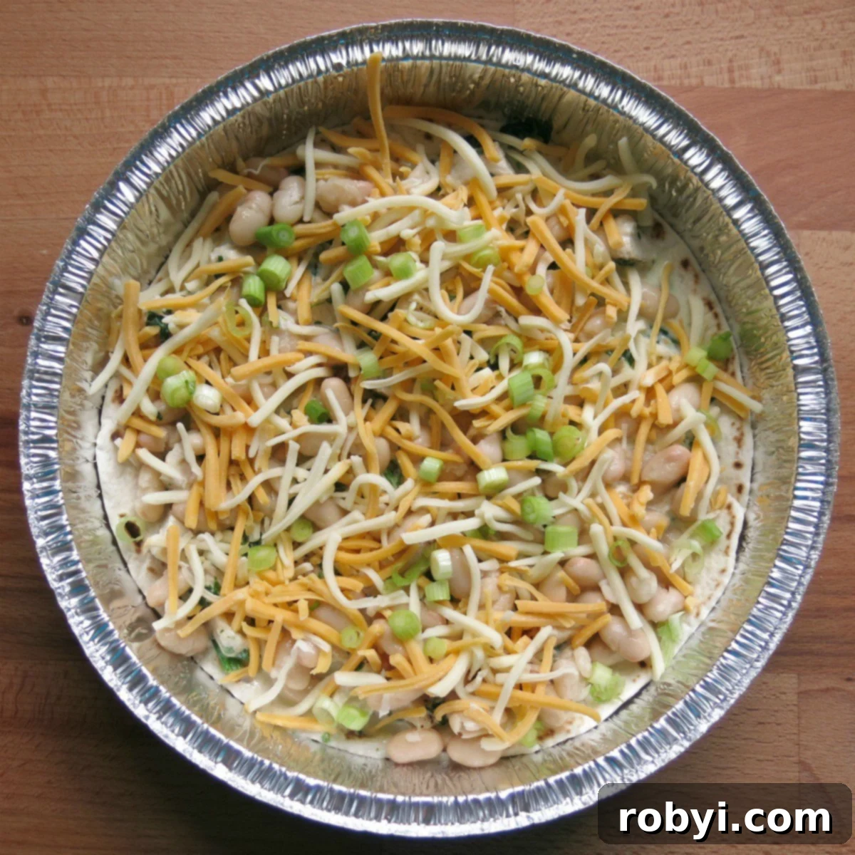 Repurpose Your Chicken Effortless Enchilada Bake 4 The first layer of creamy chicken enchilada pie in a round cake pan, showing the tortilla, sauce, chicken, beans, and cheese.