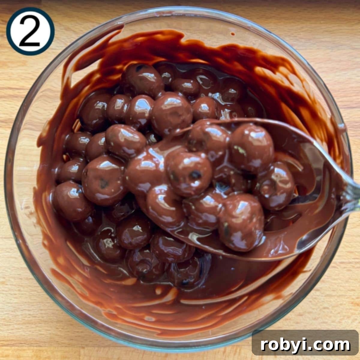 Blueberries in a glass bowl with melted chocolate and a spoon.