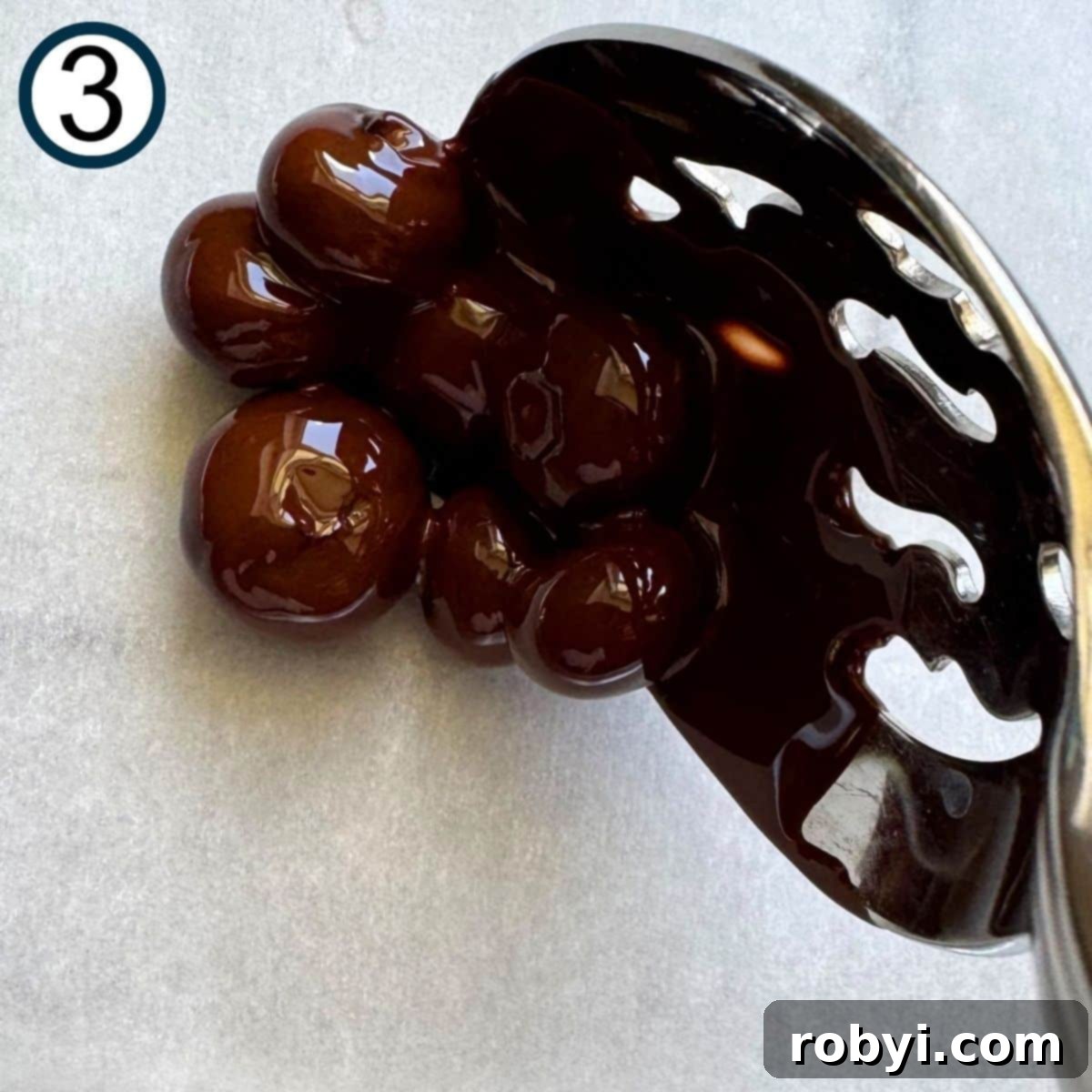 Slotted spoon lifting chocolate dipped blueberries in a cluster on parchment paper.