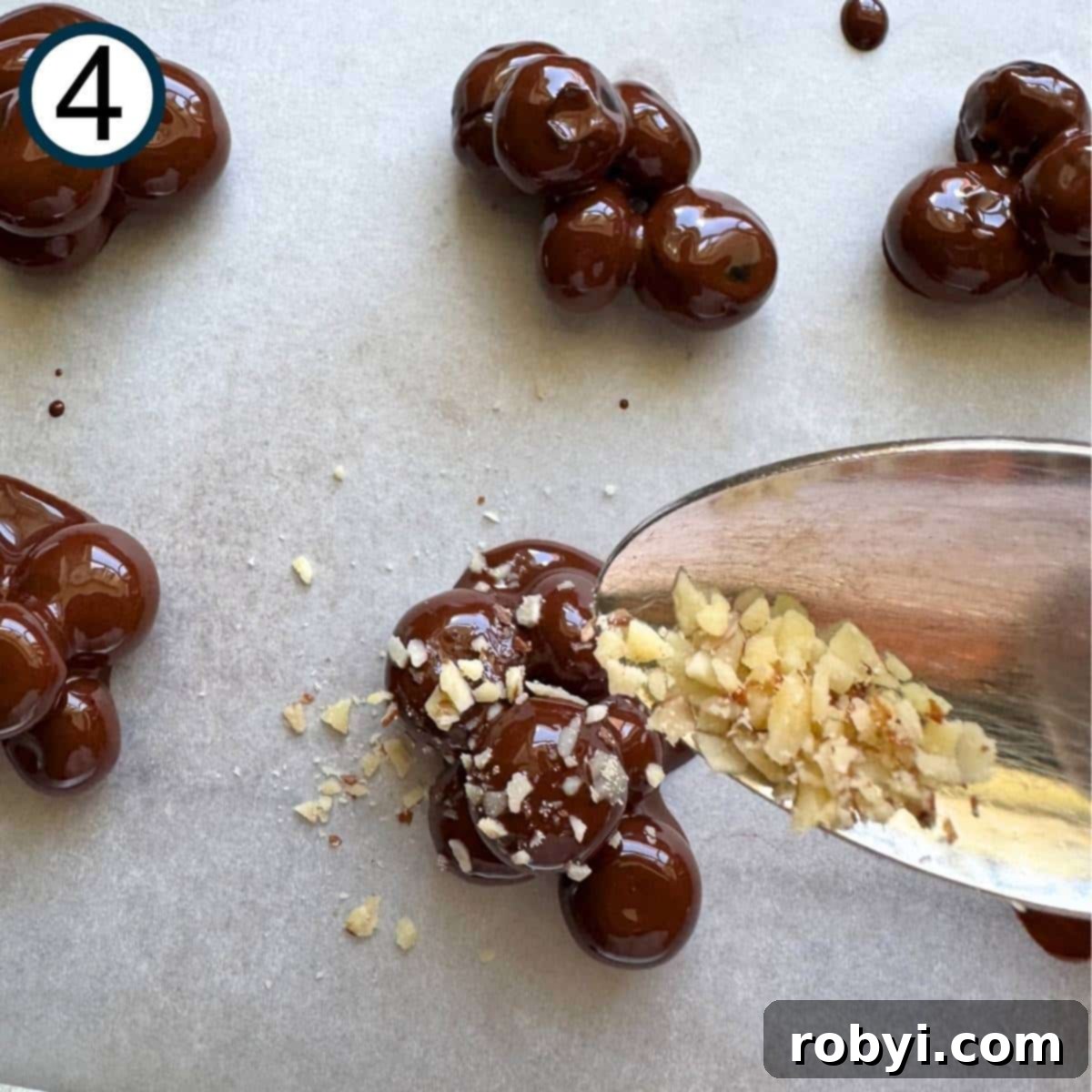 Spoon with ground almonds over a cluster of dark chocolate covered blueberries with some on top of the berries.