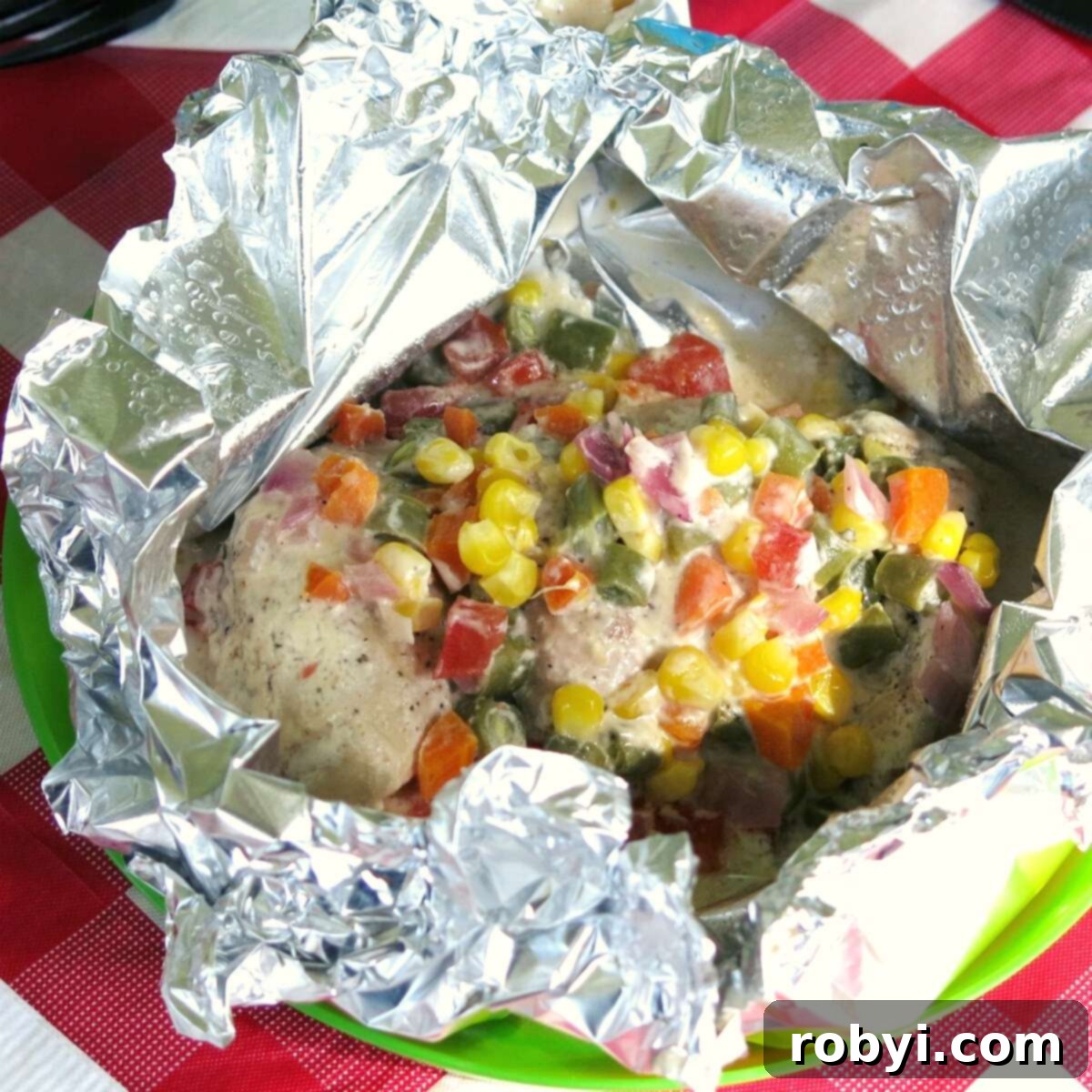 Open ranch chicken foil packets with confetti vegetables on top.