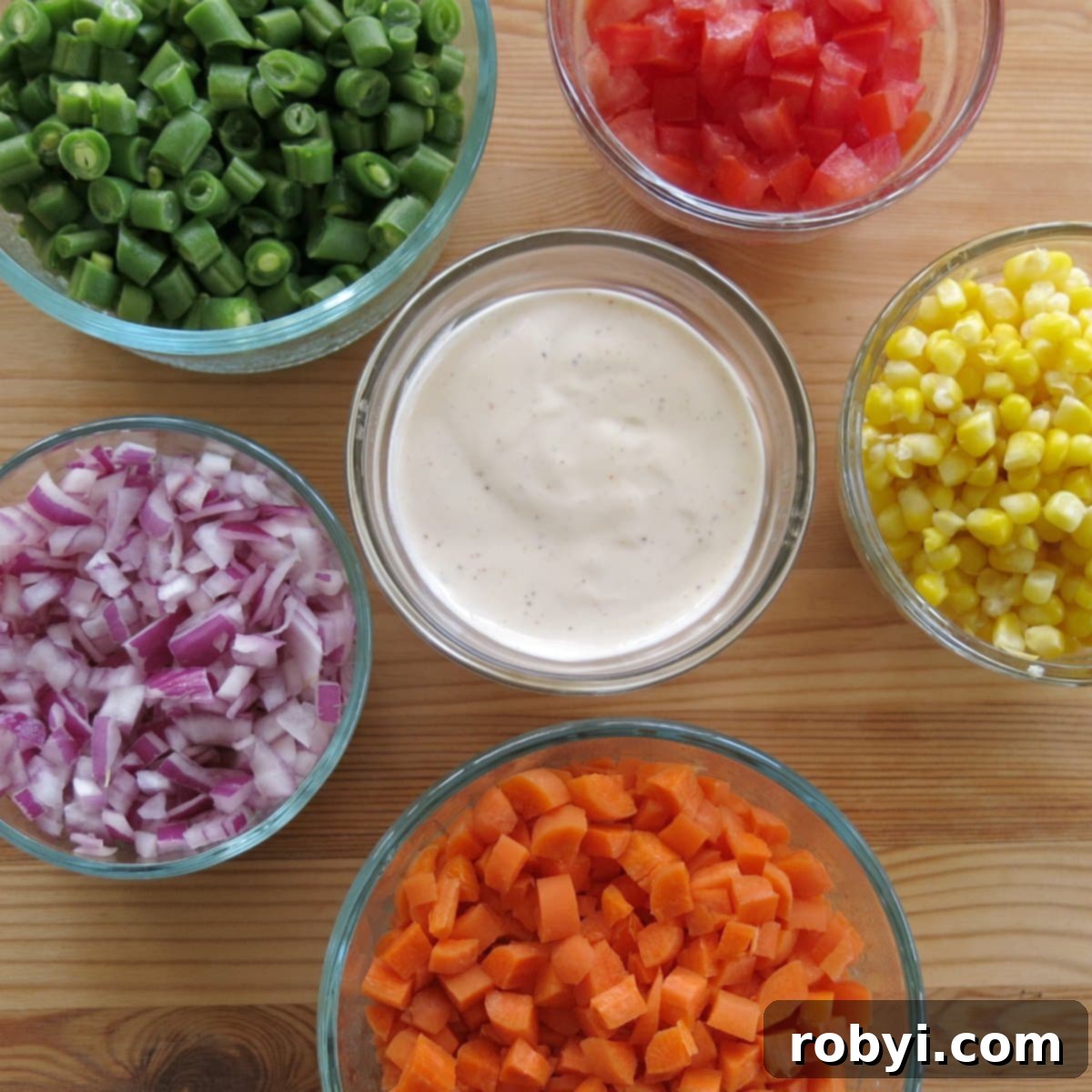 Small bowls with finely chopped vegetables surrounding a bowl of ranch dressing.