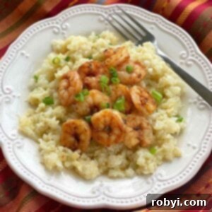 Cheesy cauliflower grits and blackened shrimp on a plate with a fork.