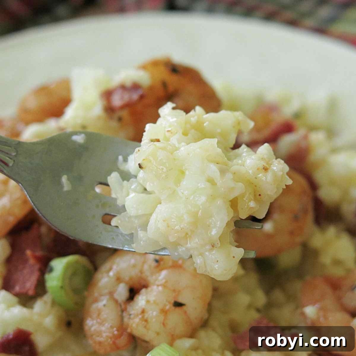 Fork holding a bite of creamy cauliflower grits, showcasing the cheesy texture.