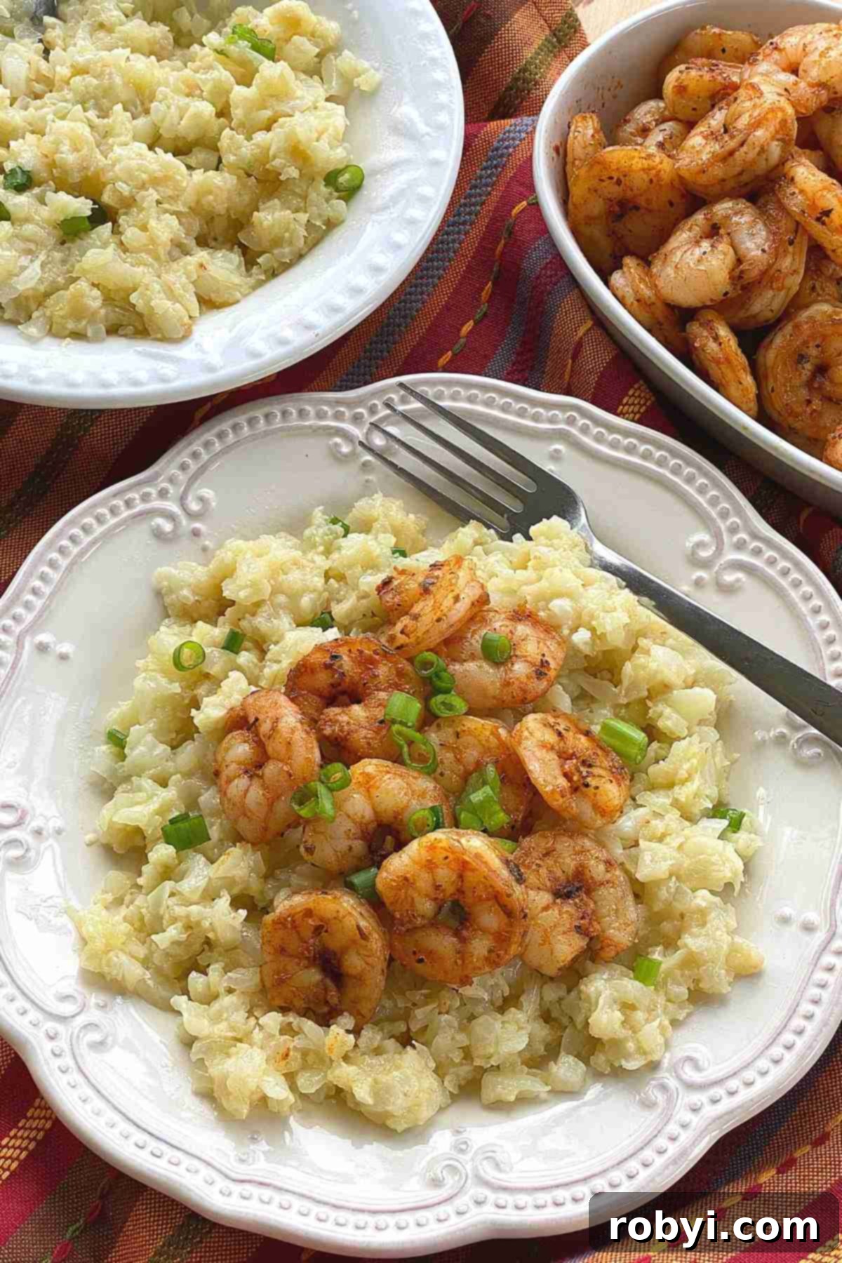 Plate with a serving of shrimp and cauliflower grits, with a bowl of each component in the background.