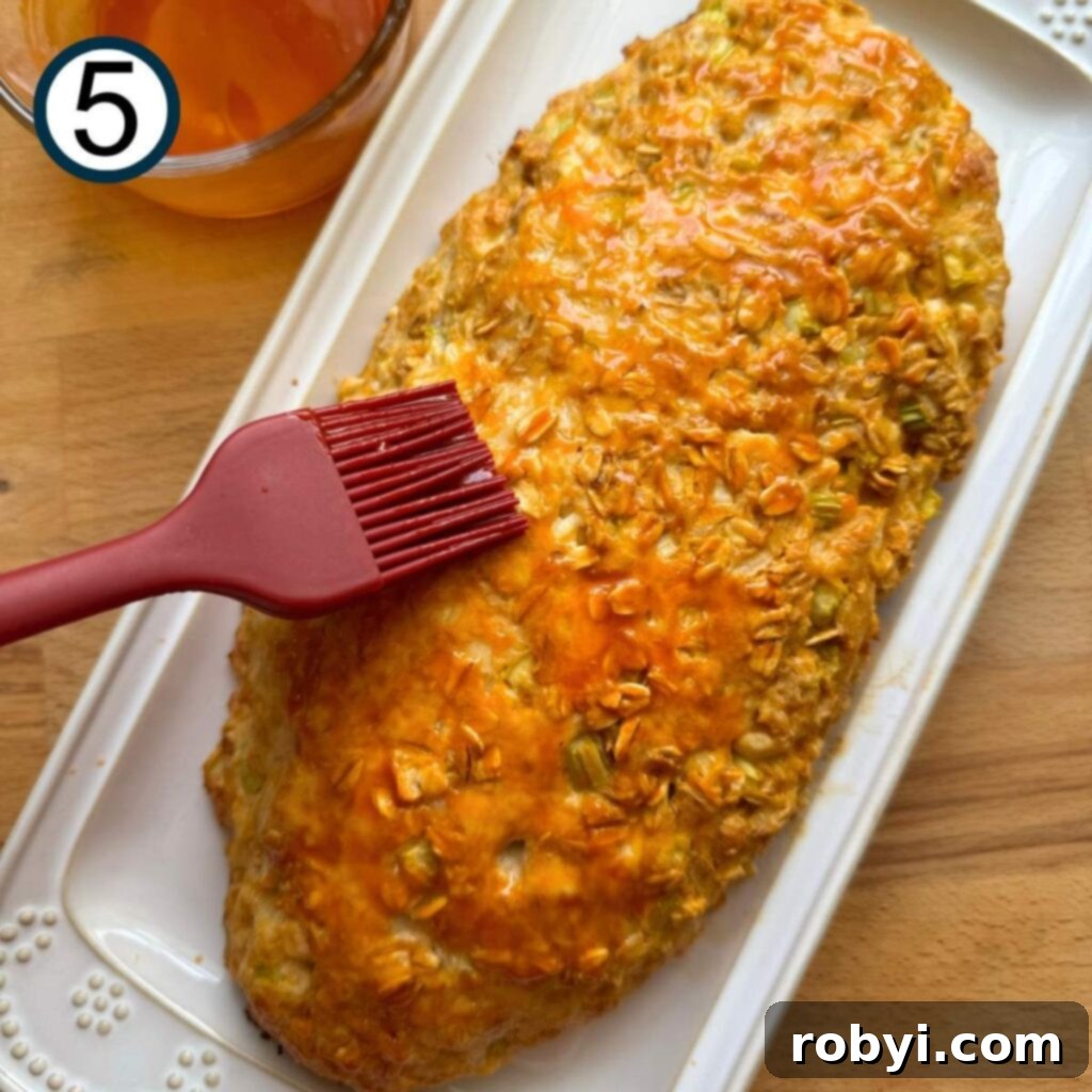 Baked buffalo chicken meatloaf on a platter with a brush adding more buffalo sauce on top.