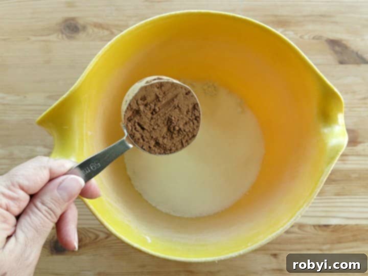 Measuring cup with cocoa powder being emptied into mixing bowl for chocolate pumpkin muffins
