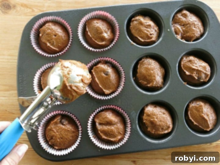 Ice cream scoop putting chocolate pumpkin muffin batter in cupcake baking pan.