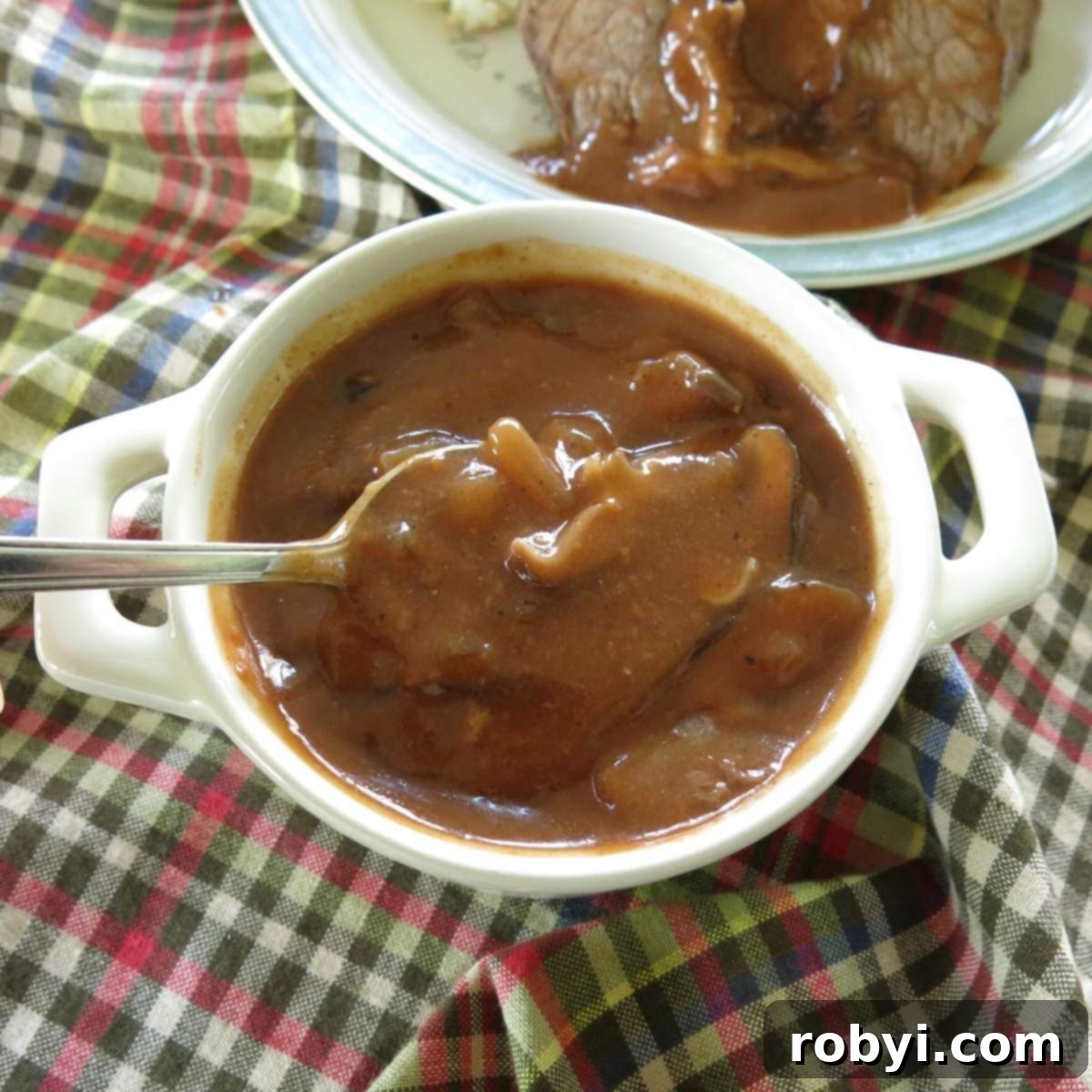 Spoonful of red wine mushroom gravy being lifted out of serving bowl.