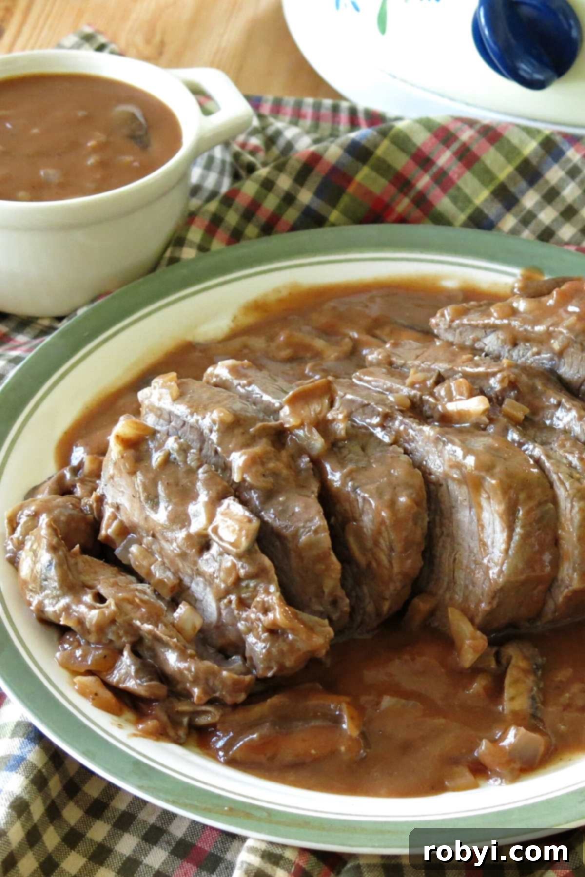 Slow Cooker Beef Shoulder Roast topped with mushroom wine sauce on plate with crock-pot behind it.