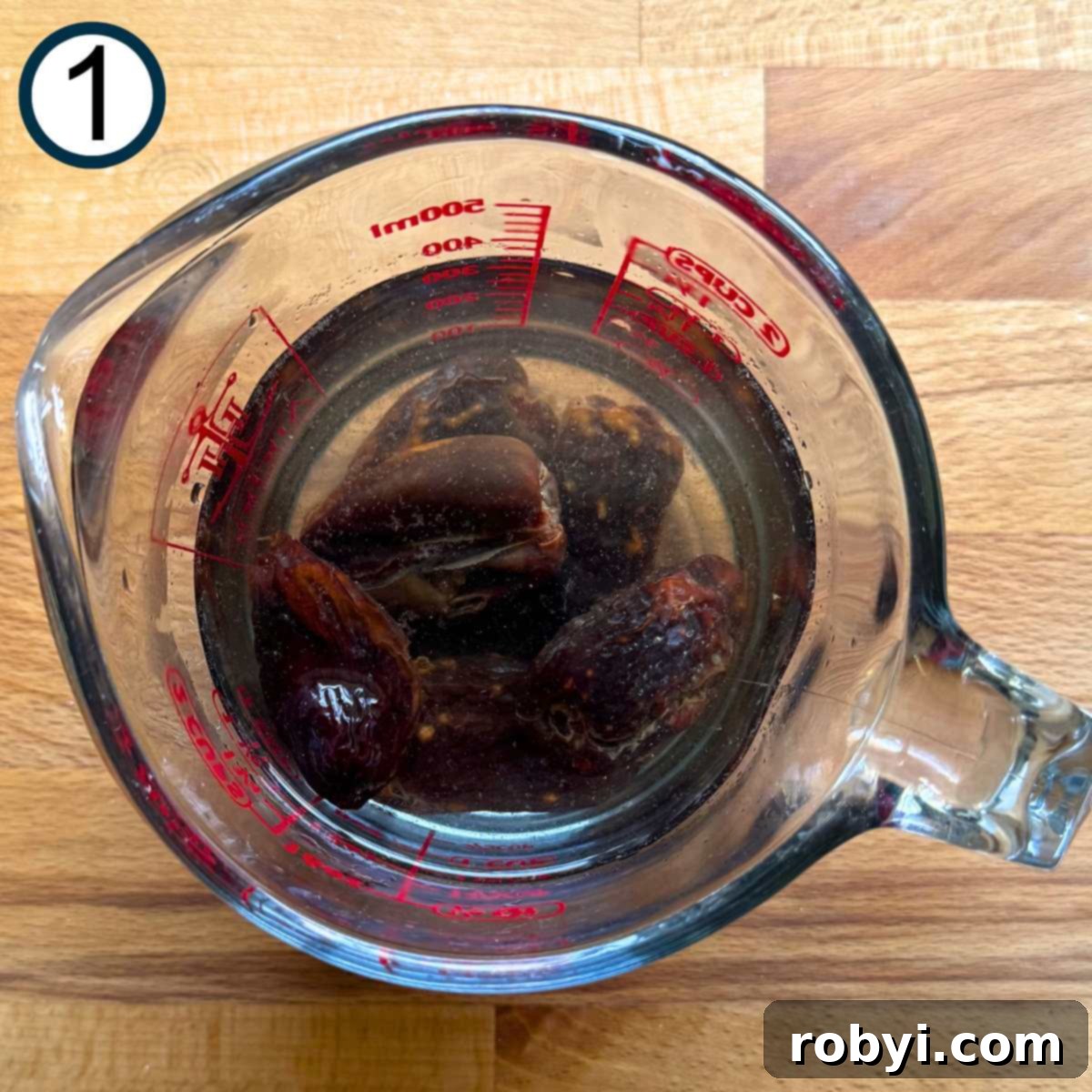 Eight pitted Medjool dates in a glass measuring cup covered with water.