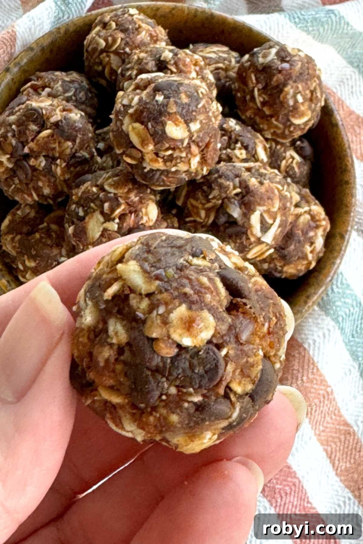 Fingers holding an energy ball made with dates and oats over a bowl with many more rolled balls.