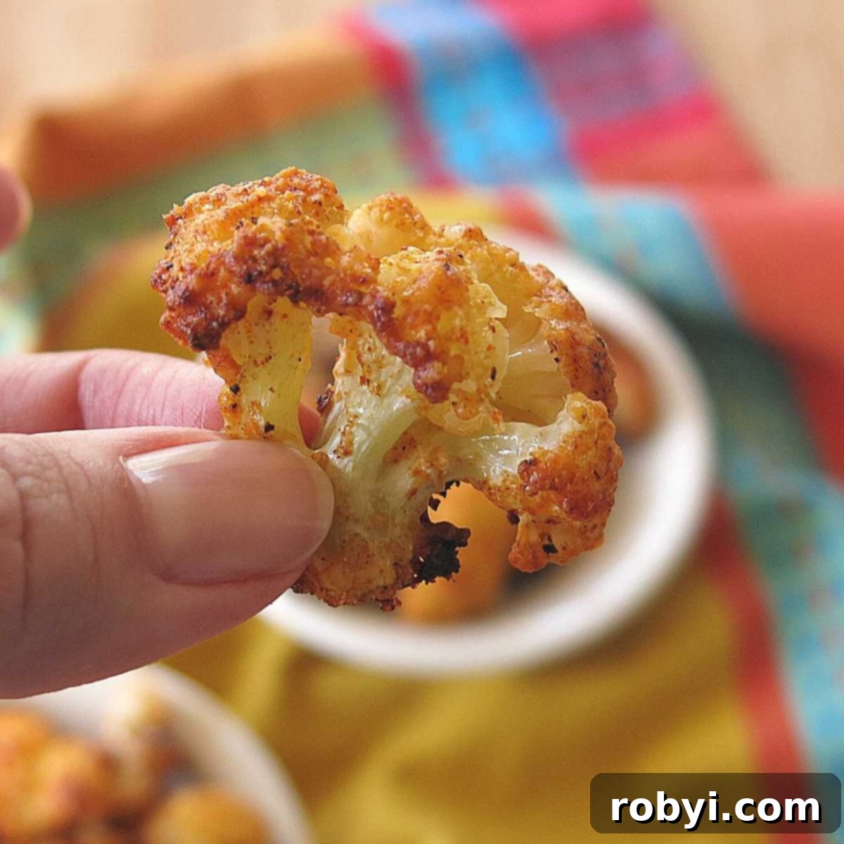5-Ingredient Parmesan Cauliflower Poppers 3 A hand holding a single Parmesan Cauliflower Bite, showcasing its crispy texture.