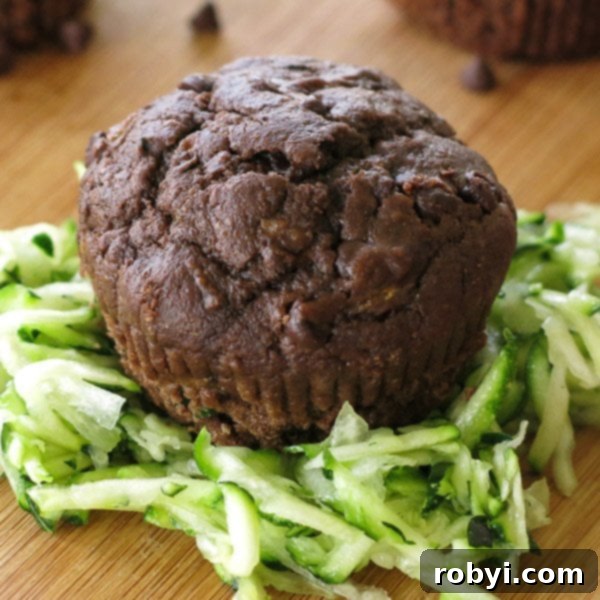 Rich chocolate zucchini muffin on a rustic cutting board, surrounded by fresh shredded zucchini, highlighting its hidden healthy ingredient.