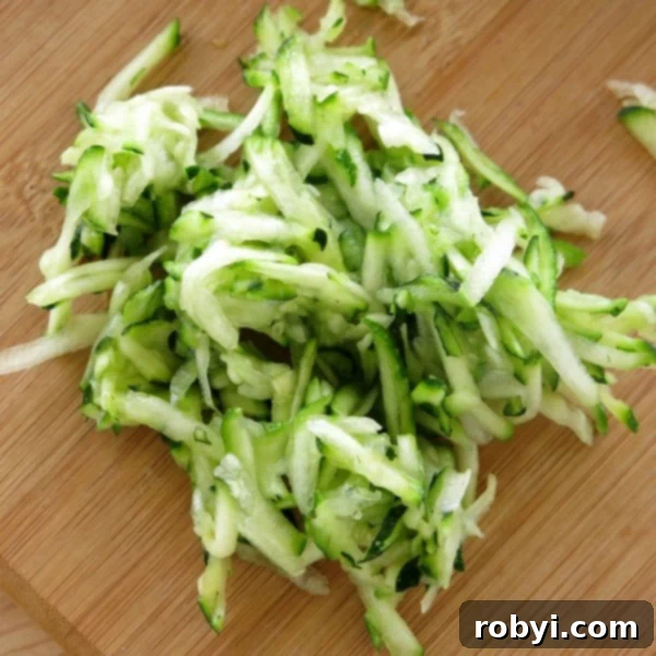 A fresh pile of finely shredded zucchini on a wooden cutting board, ready for baking.