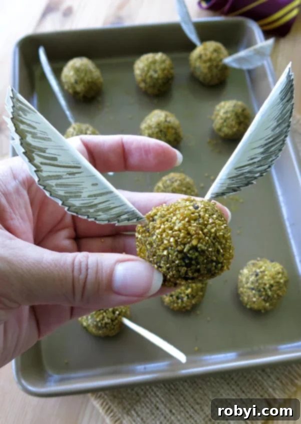 Hand holding an edible Harry Potter Golden Snitch Truffle with paper wings.