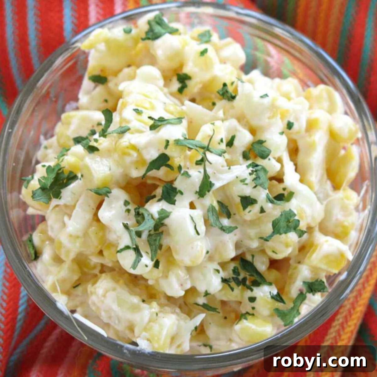 Creamy Elote Cups 2 Mexican street corn in a glass cup topped with Cotija cheese and chopped cilantro on a colorful napkin.