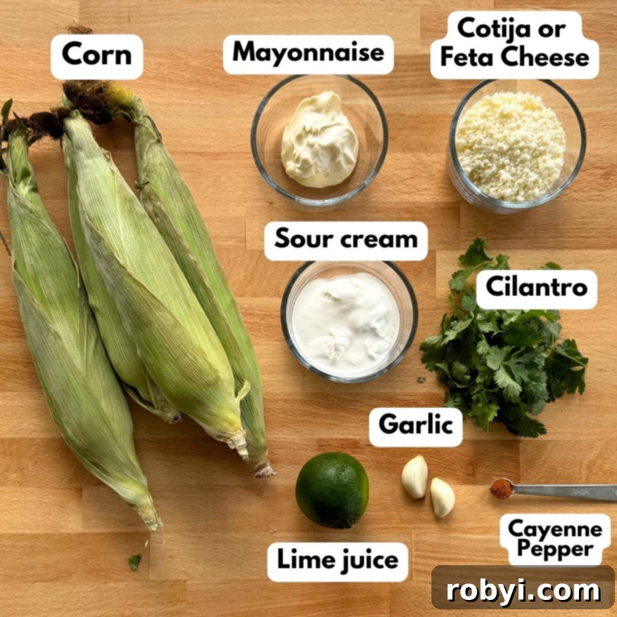 Creamy Elote Cups 3 Labeled ingredients to make the recipe: 4 cobs of corn, mayonnaise, Cotija cheese, sour cream, cilantro, 2 garlic cloves, a lime, and cayenne pepper ona measuring spoon.