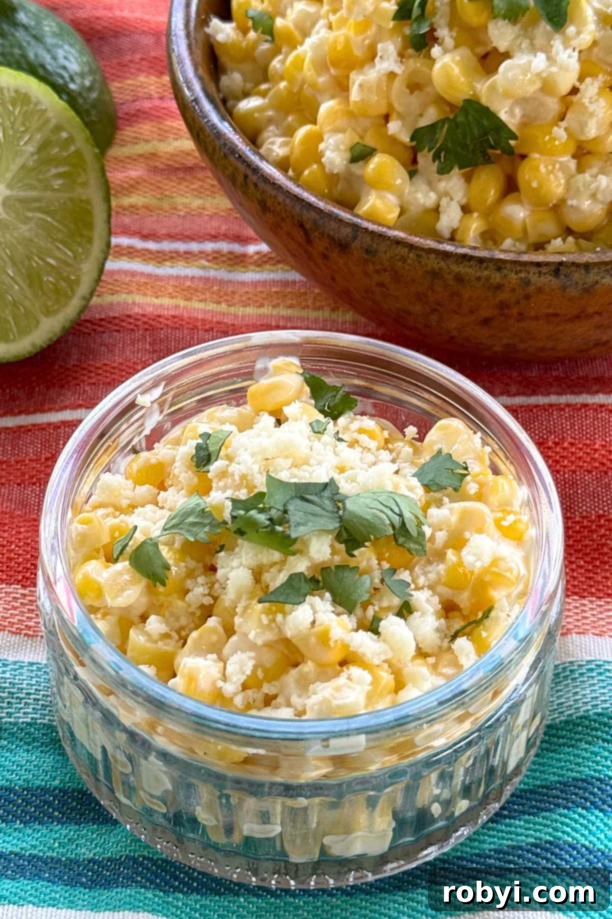 Creamy Elote Cups 8 Mexican street corn in a glass cup with a lime and a bowl with more street corn behind it.