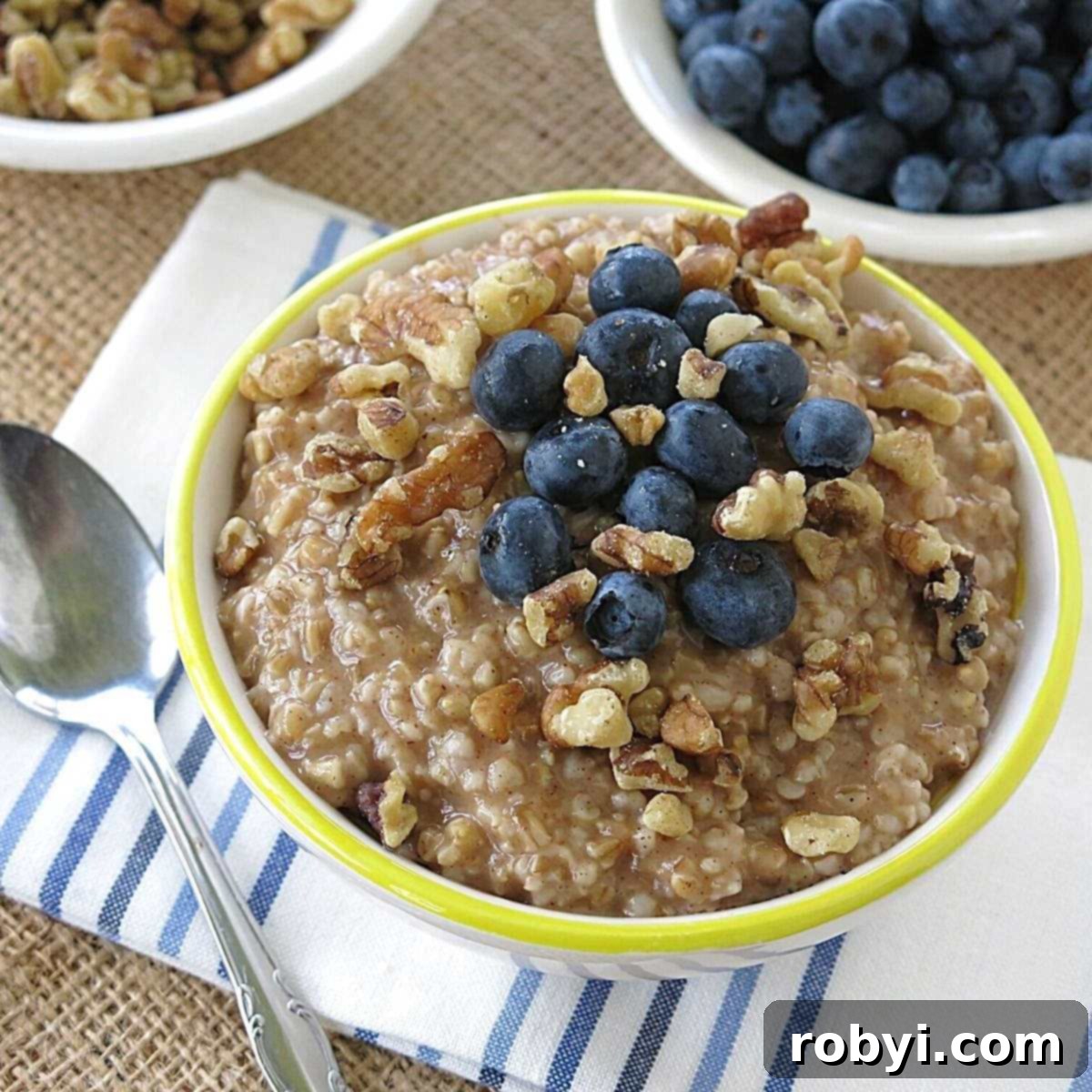 Bowl of slow cooker steel cut oatmeal with blueberries and walnuts on top and more blueberries in the background.