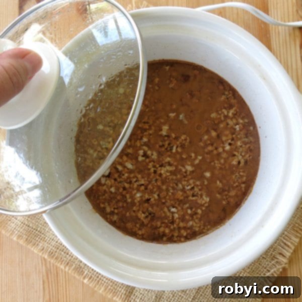 Uncooked Steel Cut Oatmeal in a CrockPot with lid partially removed.