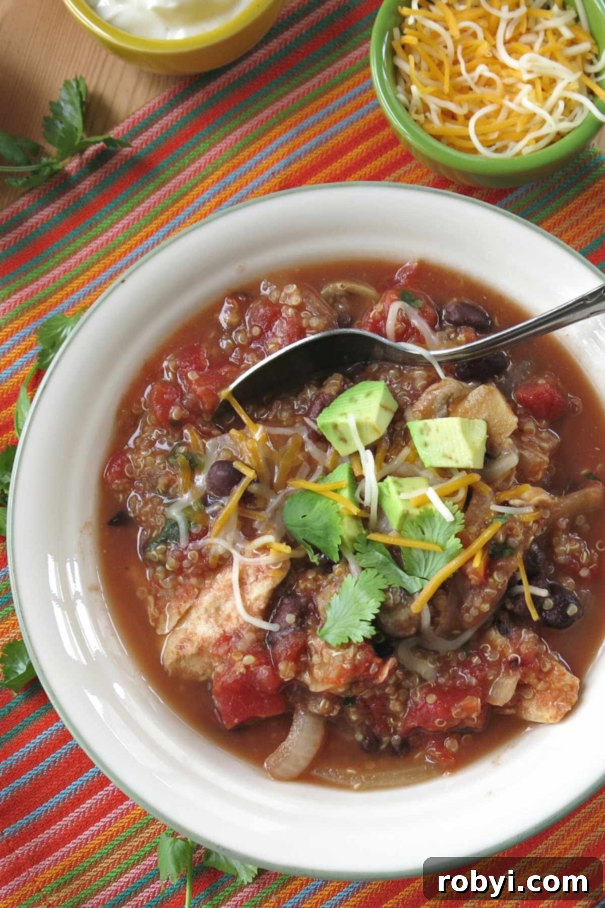 Crock-pot chicken quinoa taco soap in bowl with toppings behind it.