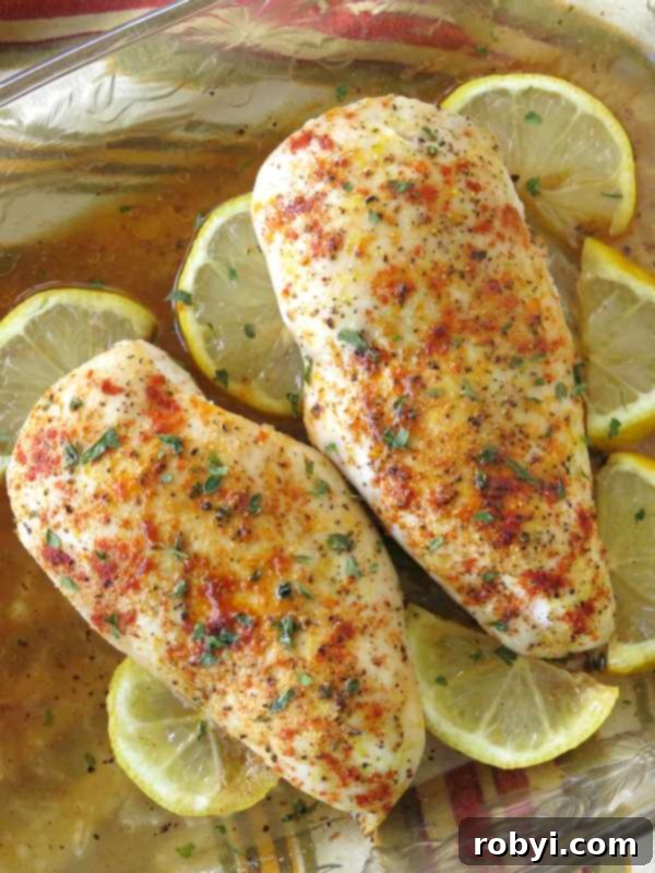 Two perfectly oven-baked Lemon Pepper Chicken breasts resting in a white baking dish, surrounded by vibrant lemon wedges, ready to serve.