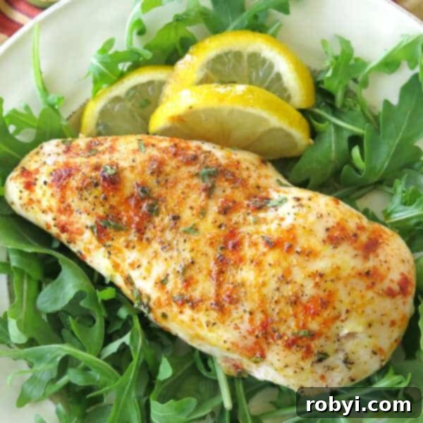 A perfectly baked Lemon Pepper Chicken breast artfully arranged on a bed of fresh greens, accompanied by bright lemon slices, highlighting its healthy and appealing presentation.