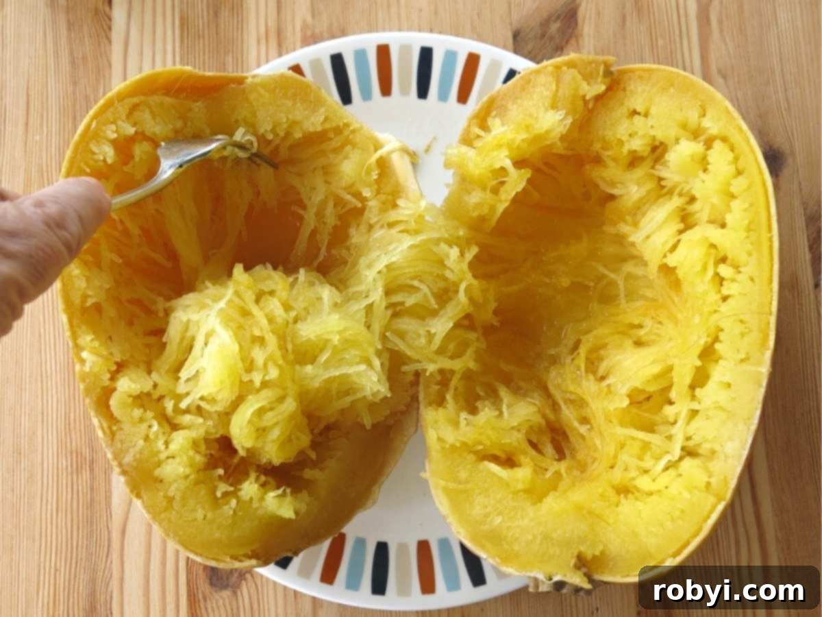 A fork skillfully scraping the long, delicate strands of spaghetti squash from the cooked gourd.