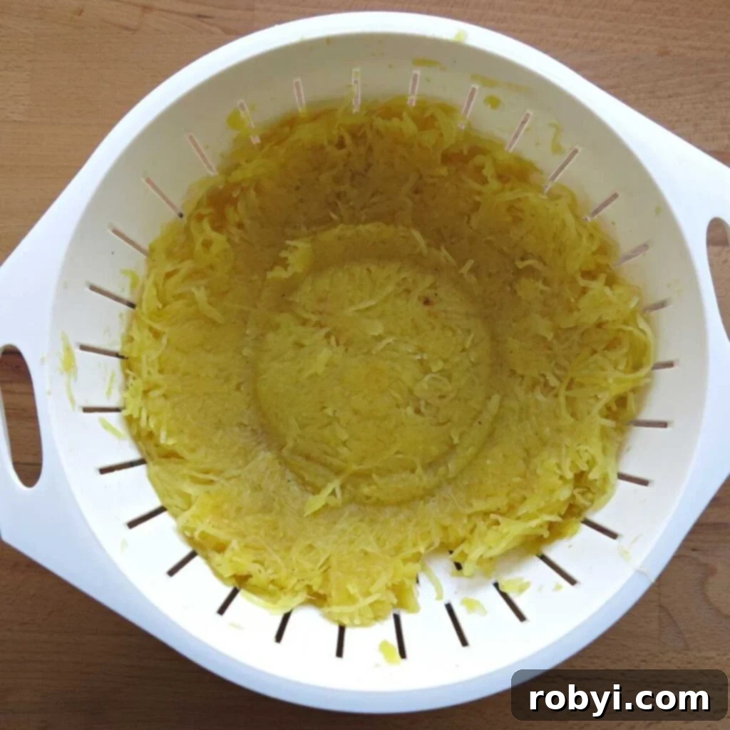 Spaghetti squash strands vigorously compressed in a strainer with a bowl on top, demonstrating the process of liquid extraction.