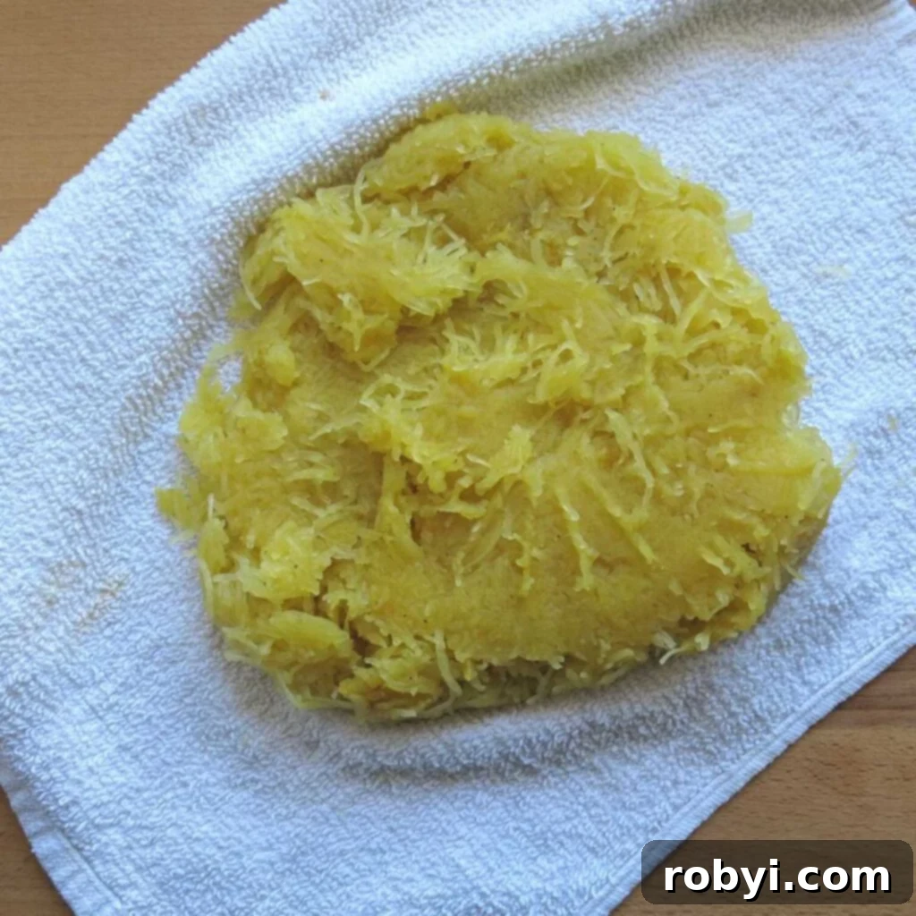 Drained spaghetti squash strands laid out on a clean dishcloth, twisted tightly to remove every last drop of moisture.