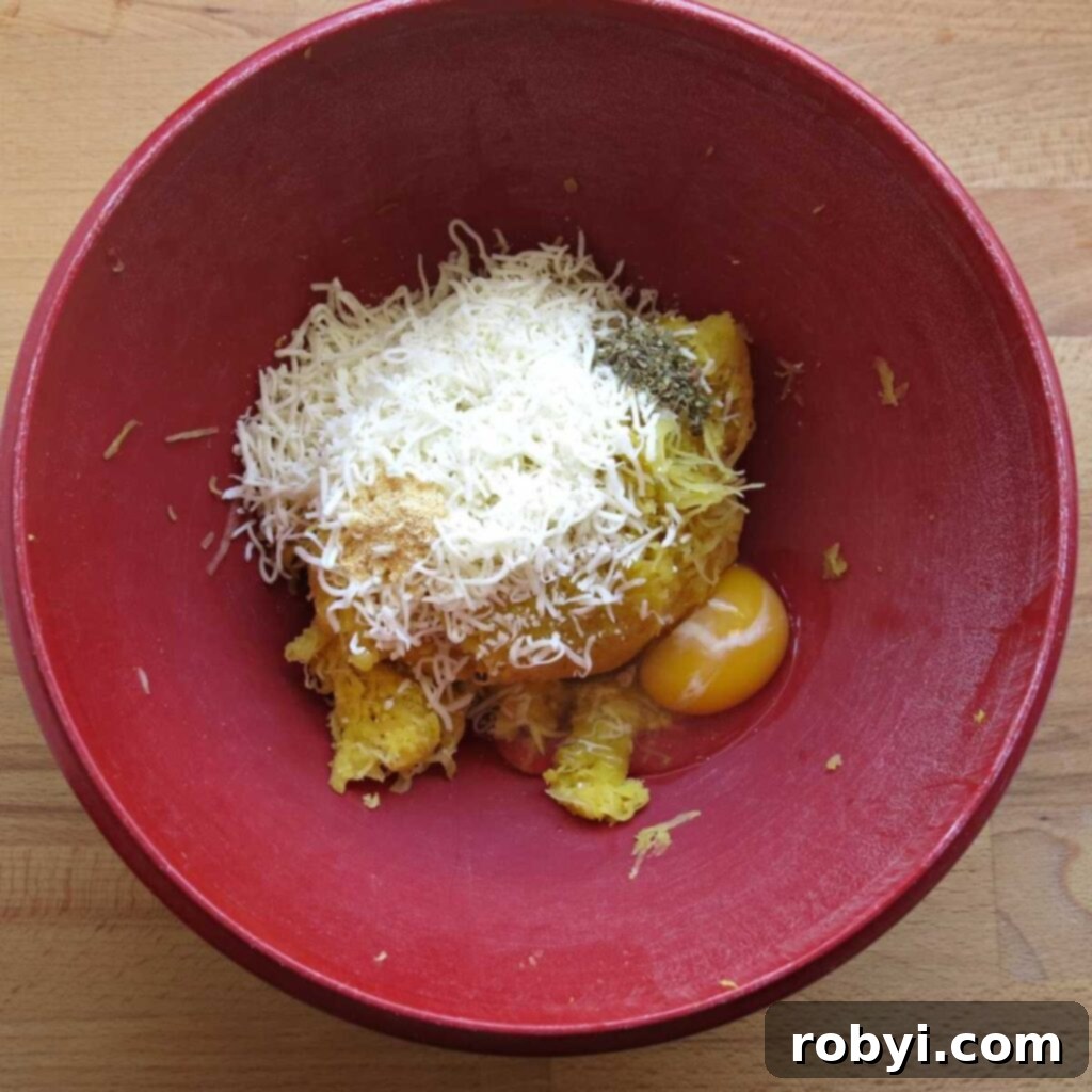 A vibrant red bowl filled with pressed spaghetti squash strands, shredded mozzarella cheese, a raw egg, and a sprinkle of oregano and garlic powder, ready to be mixed.