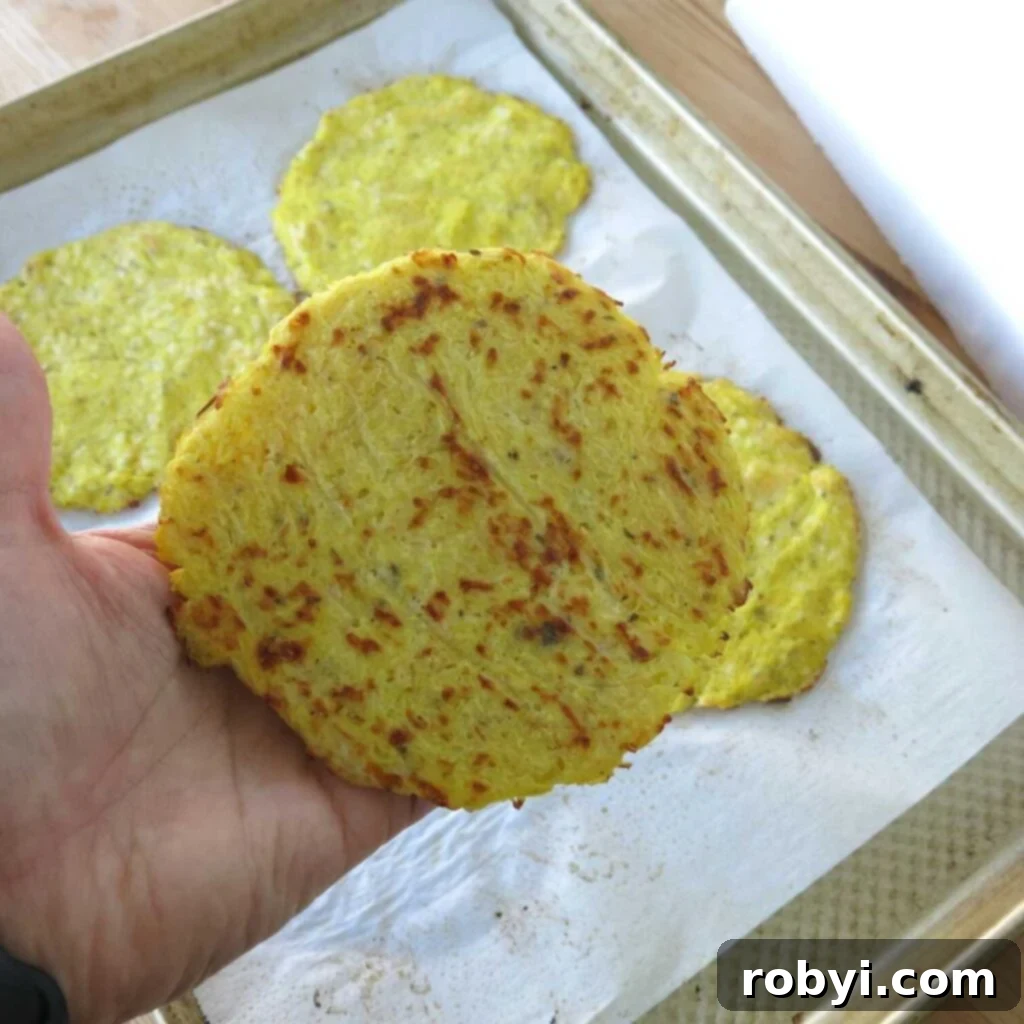 A hand gently lifts a cooked spaghetti squash pizza crust, revealing its beautifully browned and crispy underside, a sign of perfect baking.