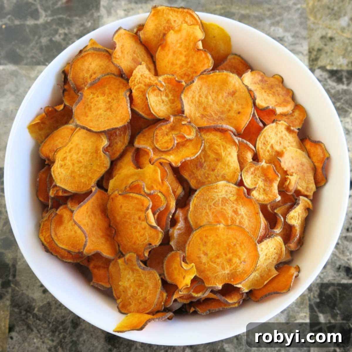 Crispy baked sweet potato chips piled high in a clean white bowl, ready to be enjoyed as a healthy snack or side dish.