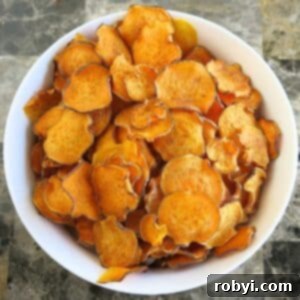 Baked sweet potato chips in a large white bowl on a marble table.