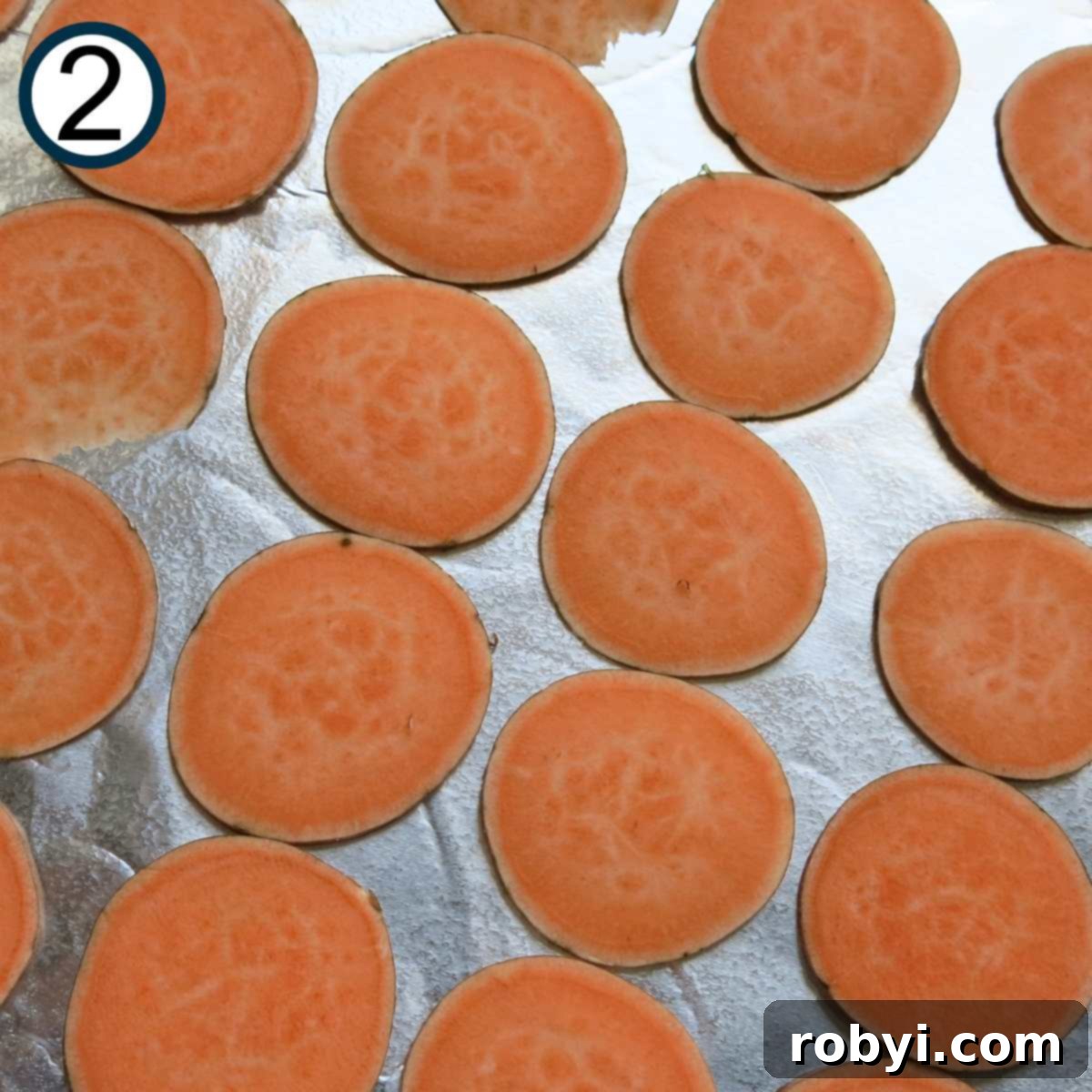 Numerous uncooked sweet potato slices meticulously arranged in a single layer on a parchment-lined baking sheet, awaiting their seasoning and oven time.