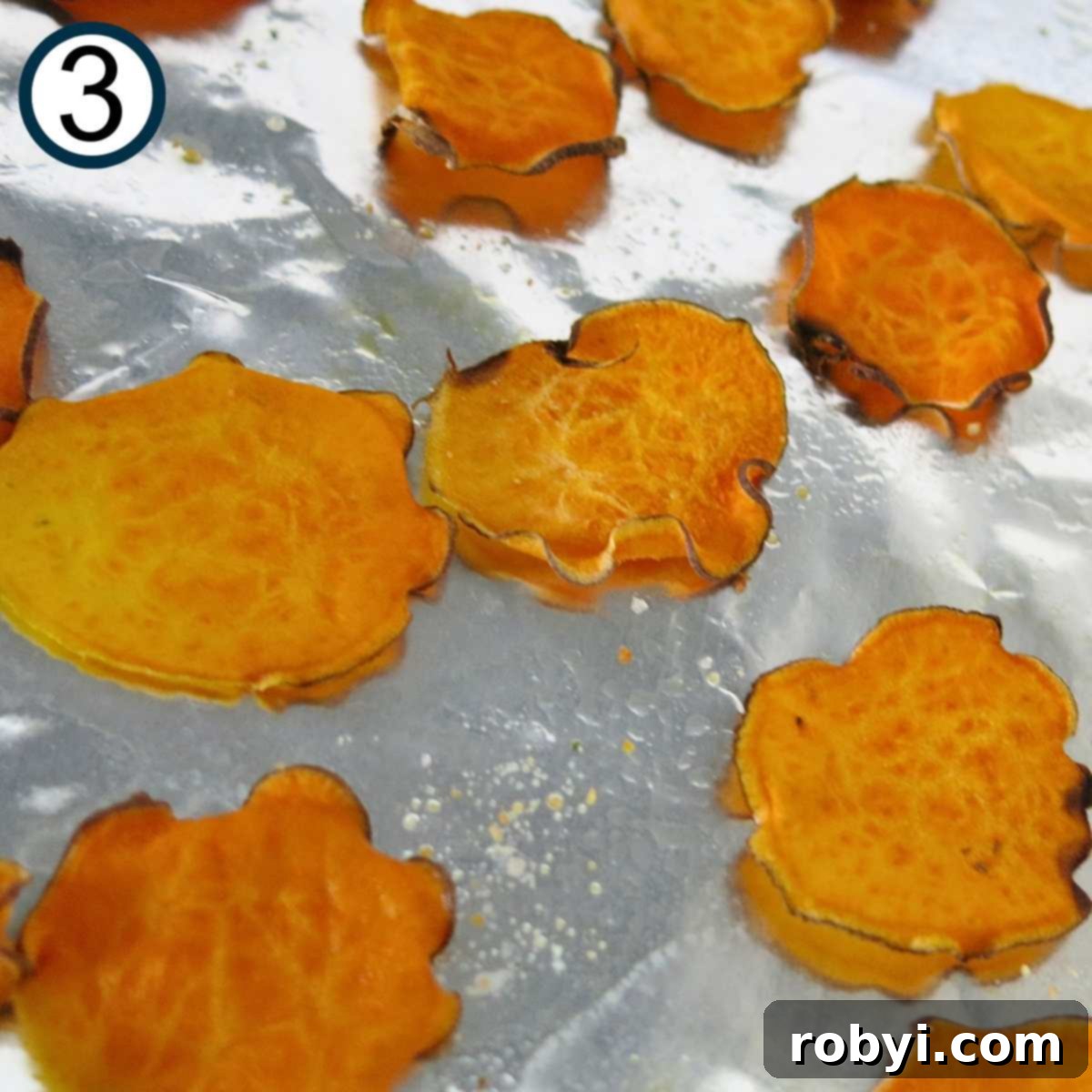 A baking sheet filled with golden-brown, baked sweet potato chips, some with edges gently curled, indicating their perfect crispness.