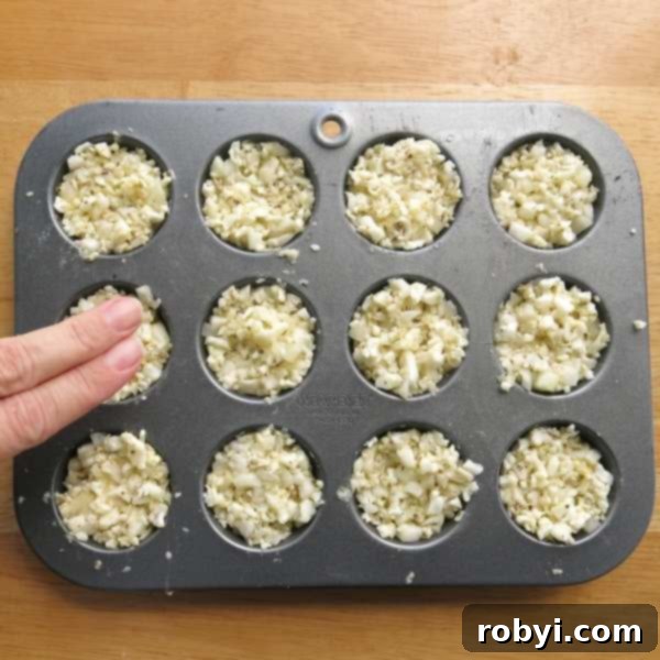Two fingers pressing down on cauliflower egg muffins to compact the mixture in a muffin tin