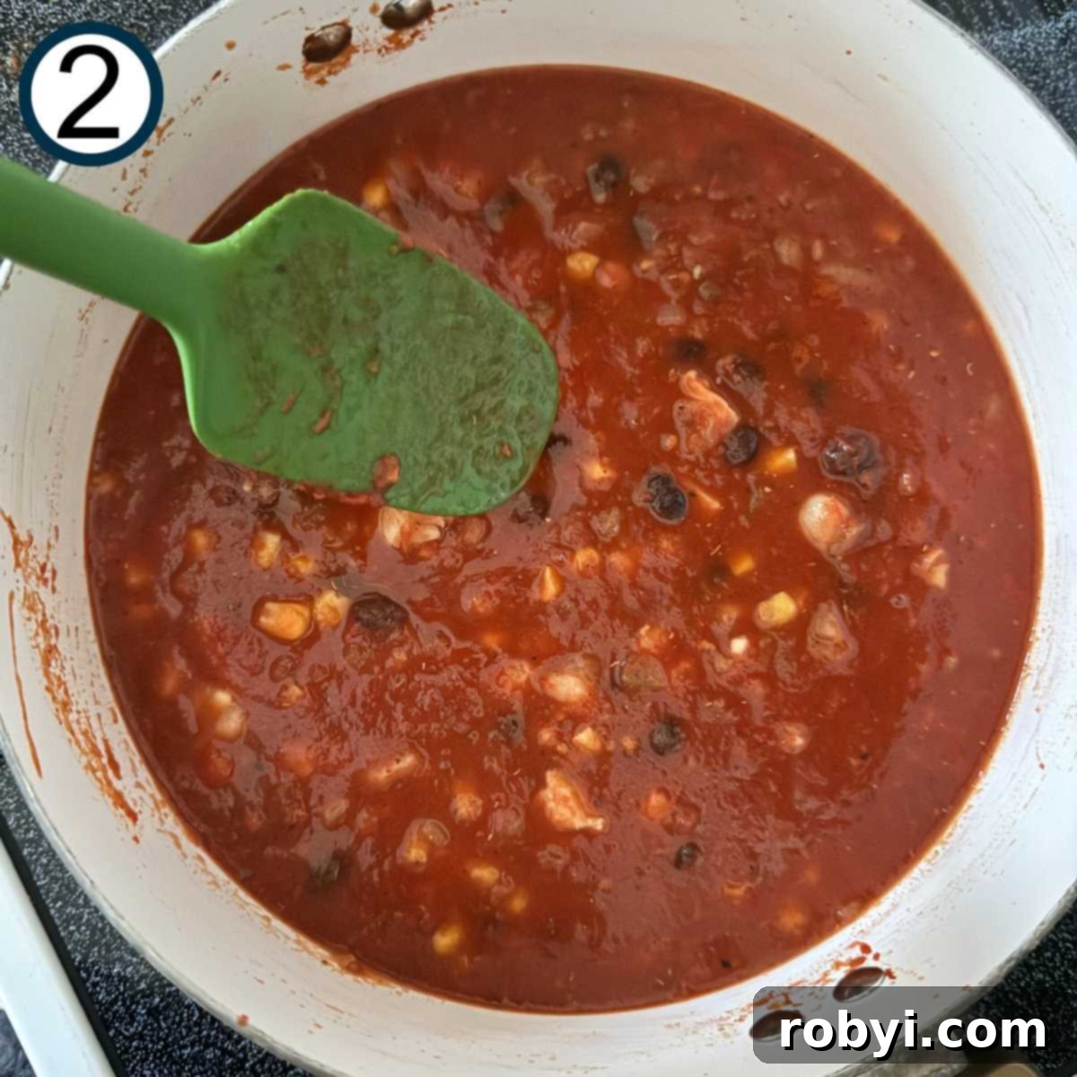 Green spatula stirring chicken tortilla soup ingredients in a pot.