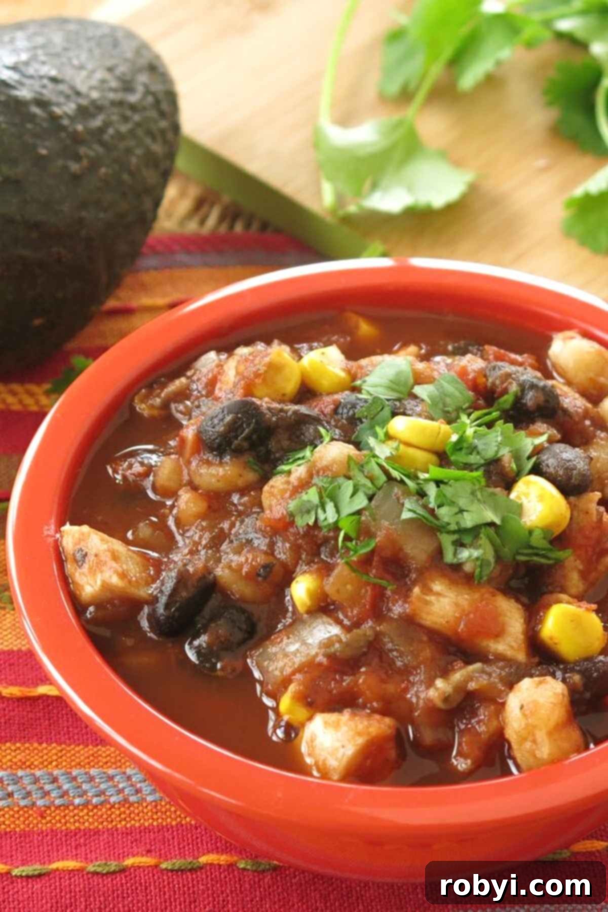Bowl of Mexican chicken tortilla soup topped with cilantro with cilantro and a whole avocado behind it.