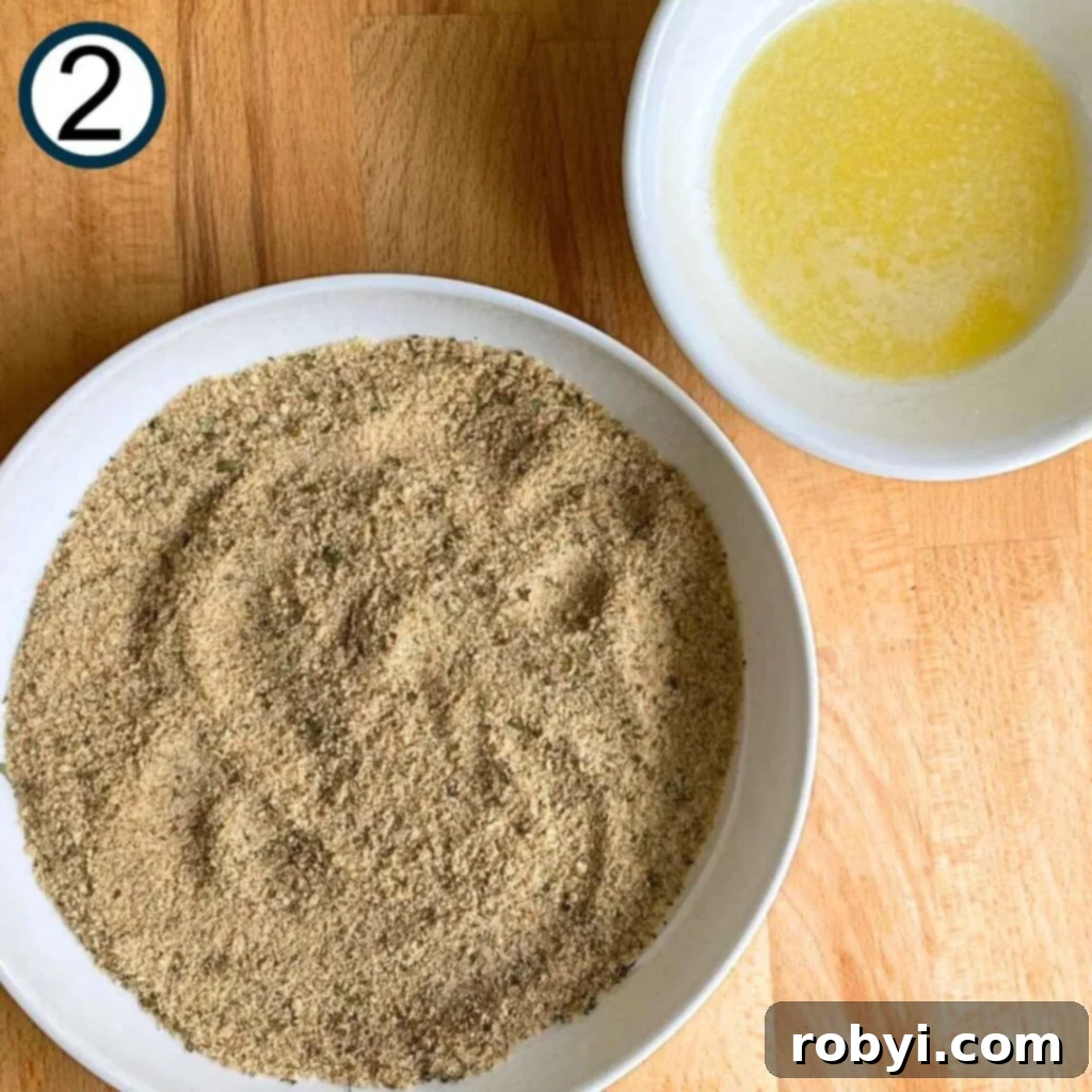 Two bowls side-by-side: one containing a melted butter and olive oil mixture, the other holding a seasoned garlic Parmesan breading.