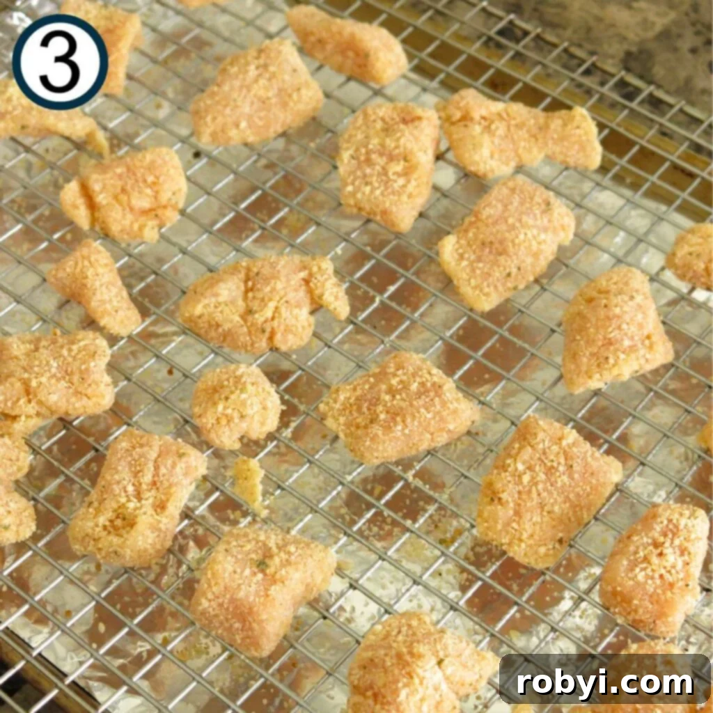 Uncooked garlic Parmesan chicken bites arranged neatly on a cooling rack set over a baking sheet, ready for baking.