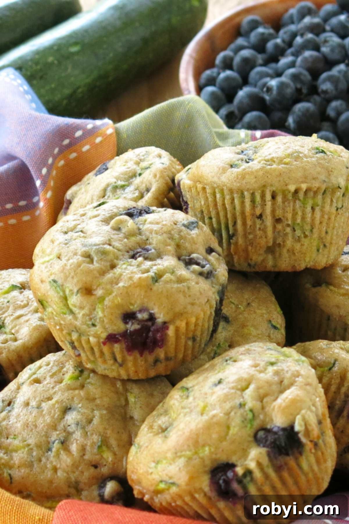 Zucchini blueberry yogurt muffins with the wrappers removed stacked in a basket with a colorful napkin.