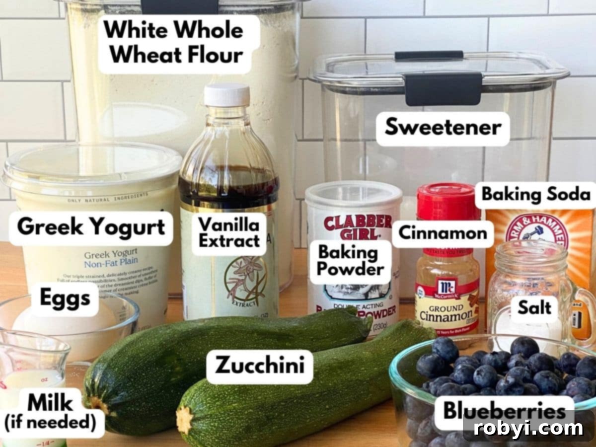 Labeled ingredients to make recipe in containers or unprocessed: white whole wheat flour, sweetener, Greek yogurt, vanilla extract, baking powder, baking soda, cinnamon, slat, eggs, zucchini, blueberries, and milk.